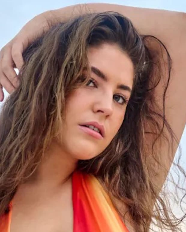 Gigi Robinson poses in a red and orange bikini with her arm over her head.